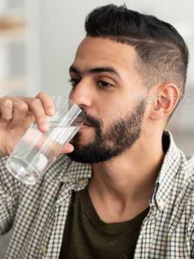 Healthy lifestyle concept. Millennial Arab guy drinking water from glass at home